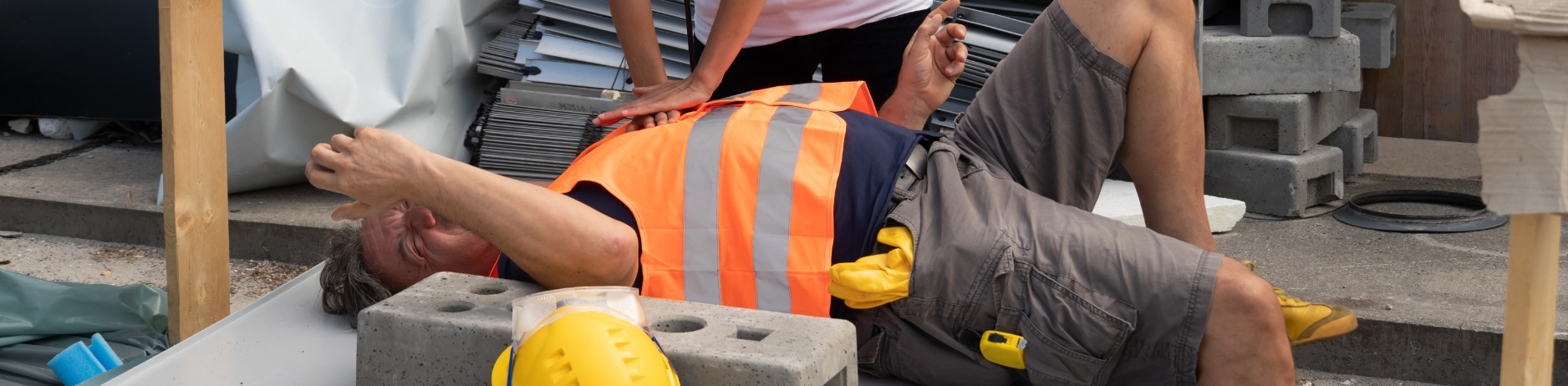 Construction worker on back in pain receiving CPR after apparent workplace accident
