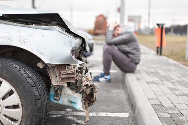 Man with head in hands by wrecked car - don't despair, maximize your car accident settlement!
